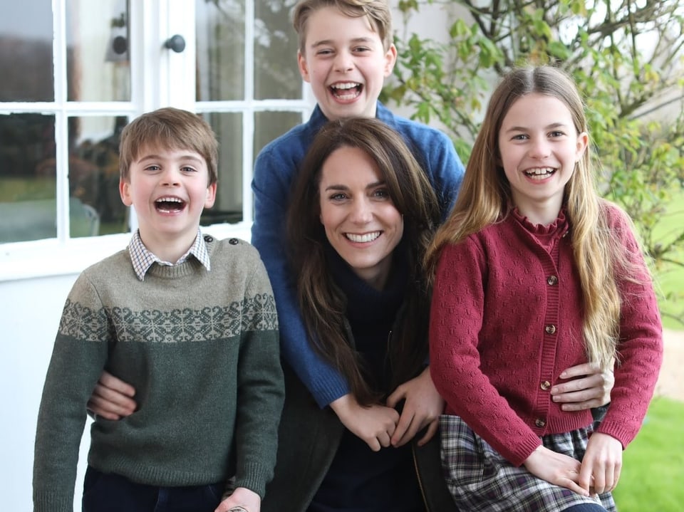 Frau mit drei Kindern, die in Kamera lächeln.