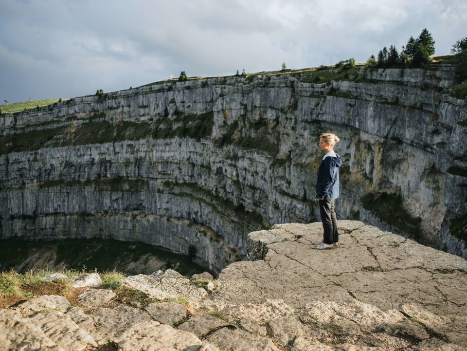 Ein Frau steht vor der steilen Felswand des Creux du Van