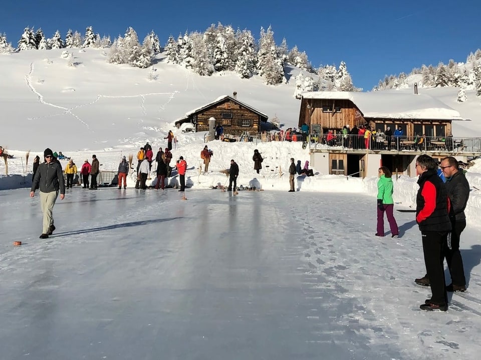 Eisfeld  mit Alphütte im Hintergrund. Menschen auf dem Eis.