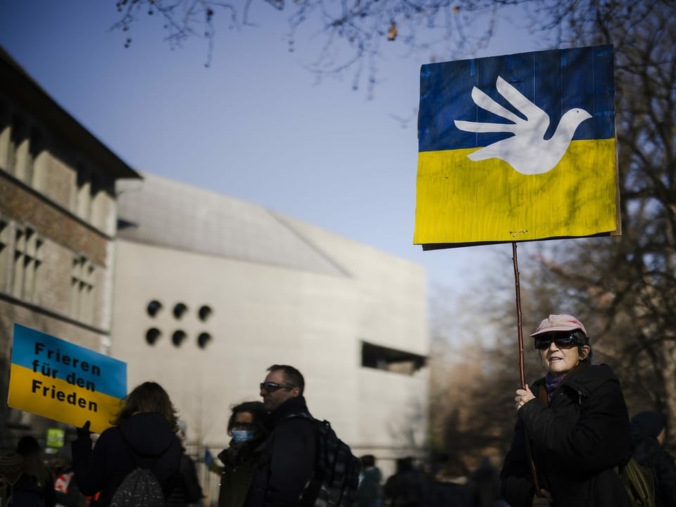 Eine Person mit einem Plakat auf dem eine weisse Taube und die ukrainische Flagge abgebildet ist. 