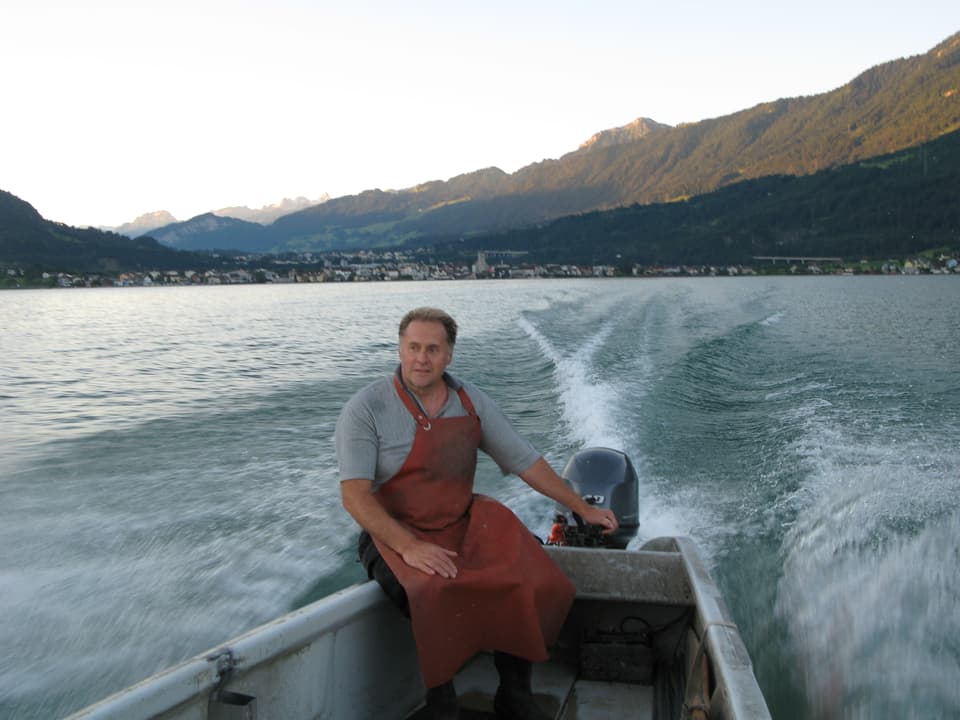 Berufsfischer Dani Schwendeler sitzt auf dem Motorboot mit roter Fischerschütze und steuert das Bott über den See.