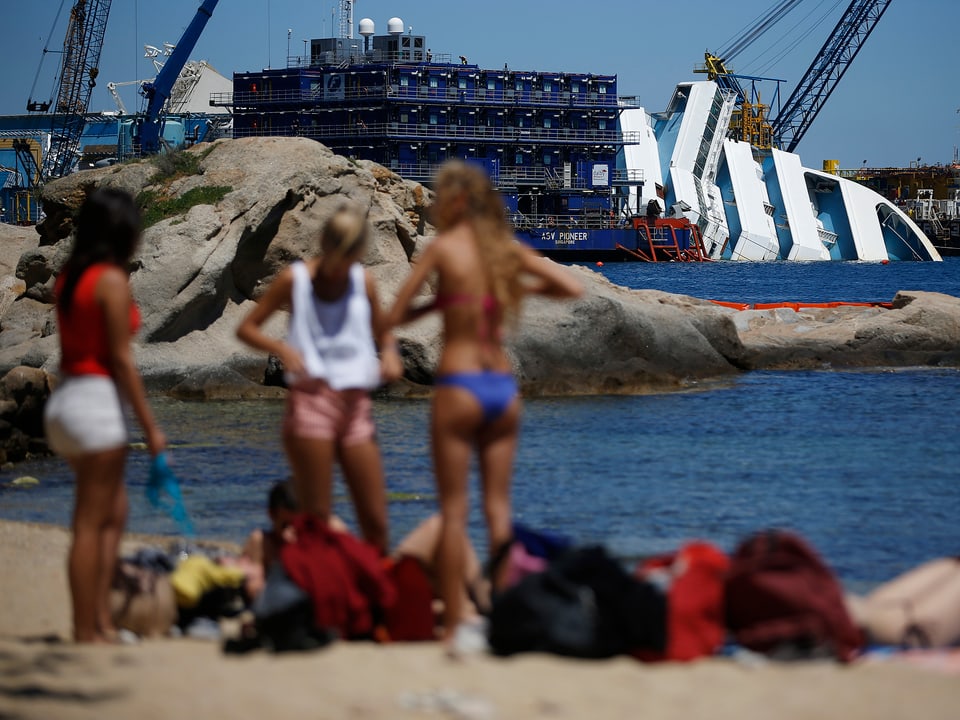 Im Vordergrund baden sich Menschen am Strand, im Hintergrund liegt das Wrack der «Concordia». (reuters)