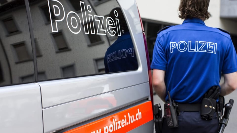 Polizist der Luzerner Polizei neben einem Patrouillenfahrzeug.