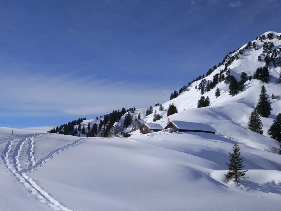 Schön verschneite Alphütte unter einem schneebedeckten Berg.