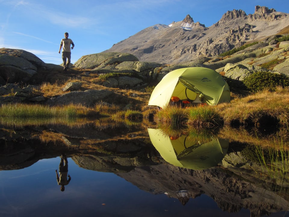 Am Bergsee steht das Zelt und im Hintergrund der Wanderer dazu.