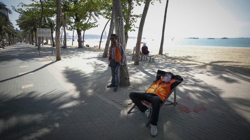 Mann mit Gesichtsmaske in einem Liegestuhl, dahinter ein leerer Strand.