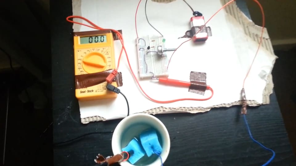 Eine Batterie, Drähte und ein Messgerät liegen auf einem Tisch.