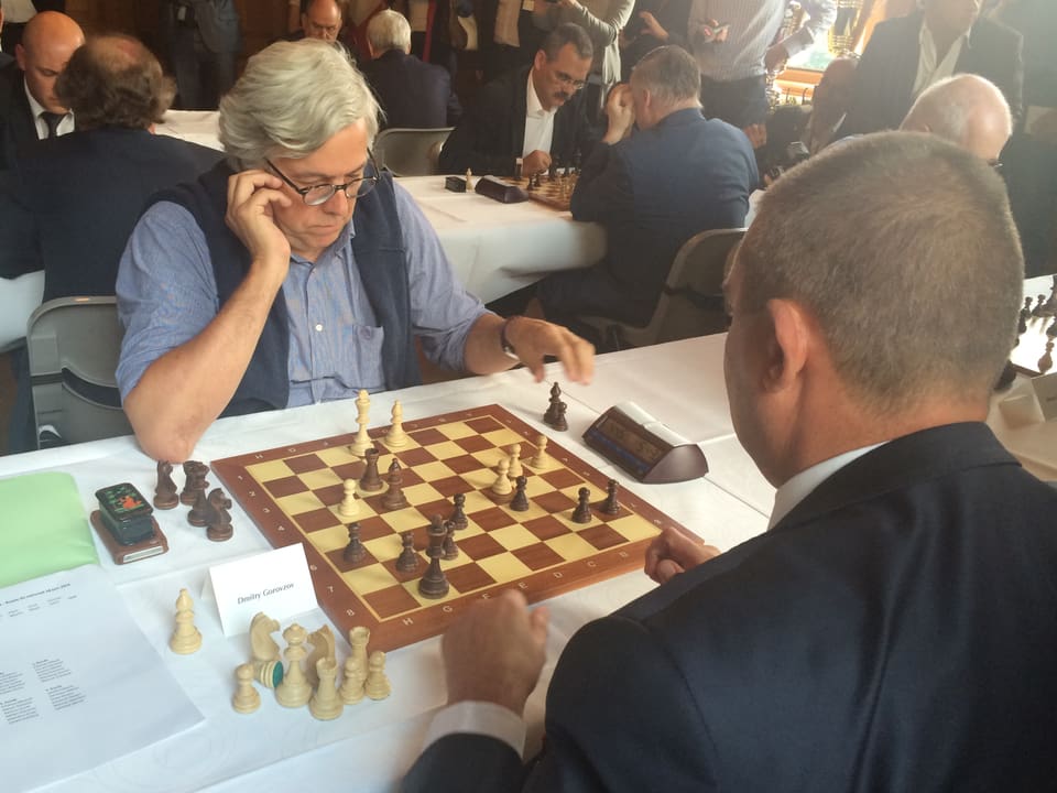 Andreas Gross, eine Hand am Ohr, eine greift nach einer Schachfigur.