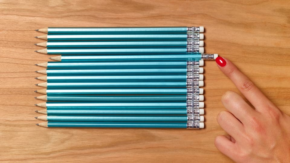 mehrere blaue Bleistifte in einer Reihe, ein einzelner steht etwas nach rechts, andere bündig. Finger rückt ihn zurecht