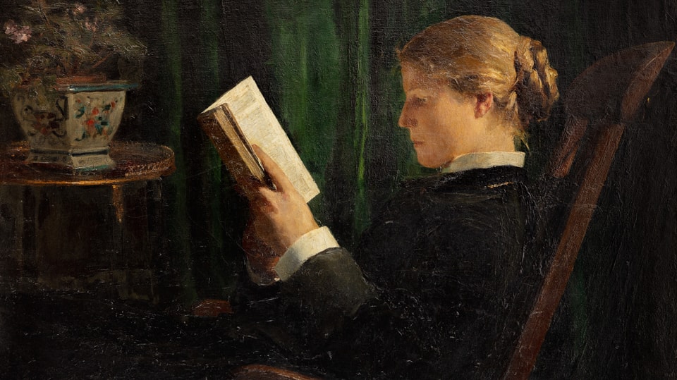 Eine junge Frau in schwarzer Kleidung sitzt auf einem Stuhl und liest. Sie ist im Profil gezeigt.