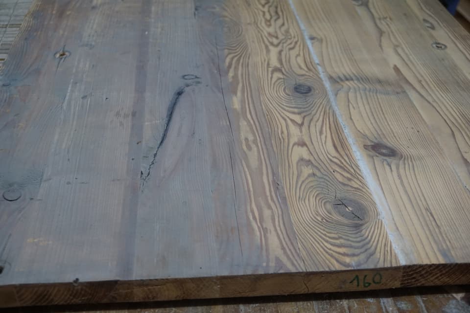 Sicht auf eine Holzplatte. Die linke Seite ist vergraut, während die Holzstruktur rechts ist wieder gut zu sehen ist.