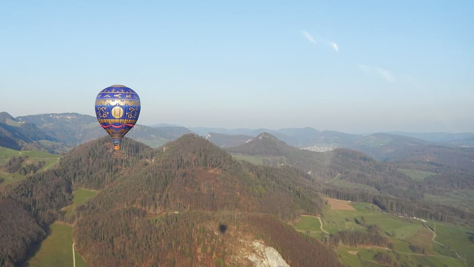 Hügelige Landschaft bei wolkenlosem Wetter. Recht klein ist ein Heissluftballon sichtbar. 