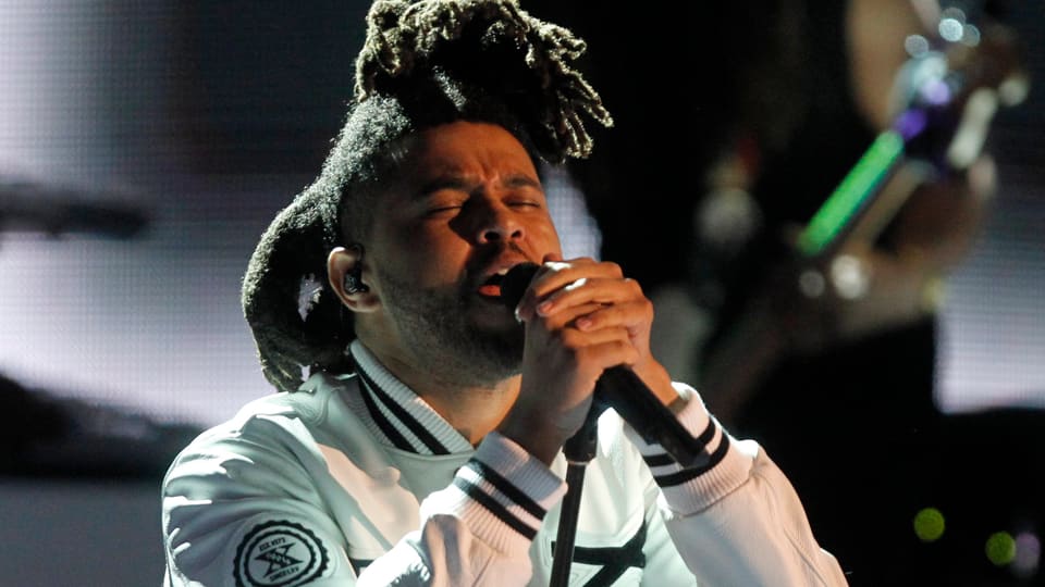 The Weeknd bei einem Bühnenauftritt, singend am Mikrofon-Ständer. 