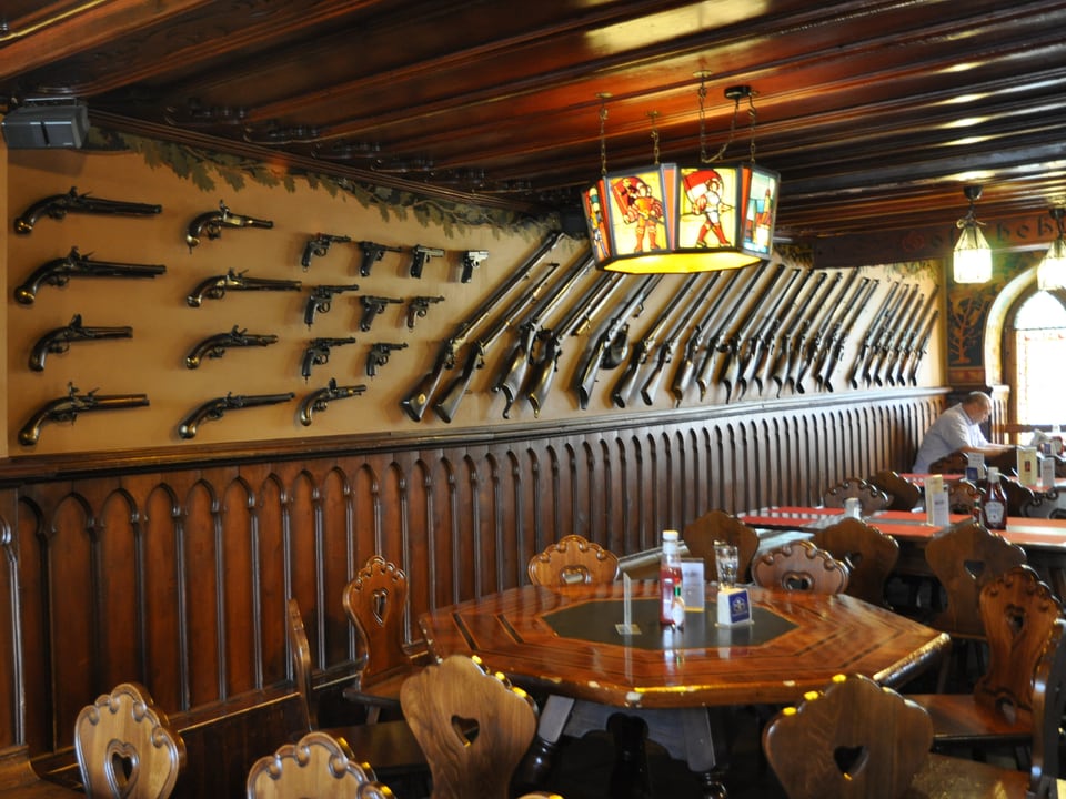 Restaurant innen, Gewehre an der Wand, Holztische und Stühle.