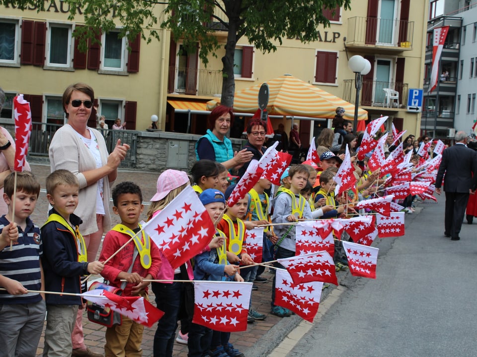 Kinder mit Walliser Fahnen stehen am Strassenrand.