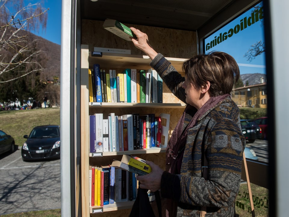 Eine Frau nimmt Bücher aus einer Mini-Bibliothek im Tessin.