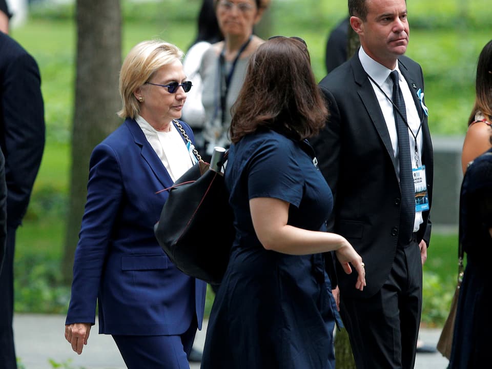 Hillary Clinton mit dunkler Sonnenbrille an Gedenkfeier. 
