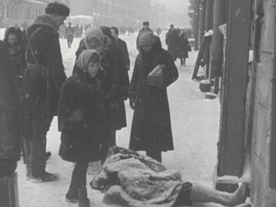 Menschengruppe steht auf schneebedeckter Strasse um eine Leiche.
