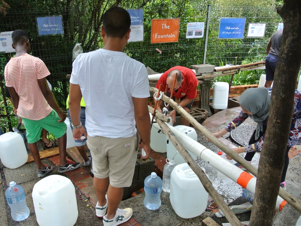Männer und Frauen füllen Wasserkanister.