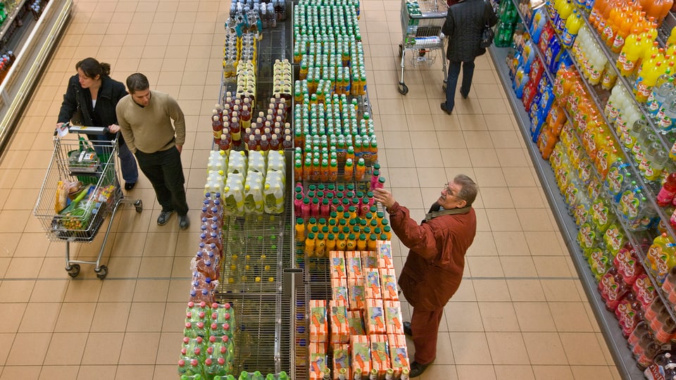 Getränkeregale in einem Supermarkt, ein Paar mit einem Einkaufswagen, ein Mann nimmt eine Flasche aus dem Regal.