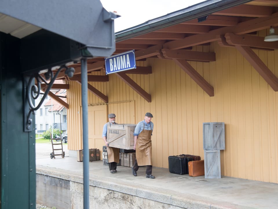 Zwei Männer tragen Holzkiste am Bahnhof Bauma