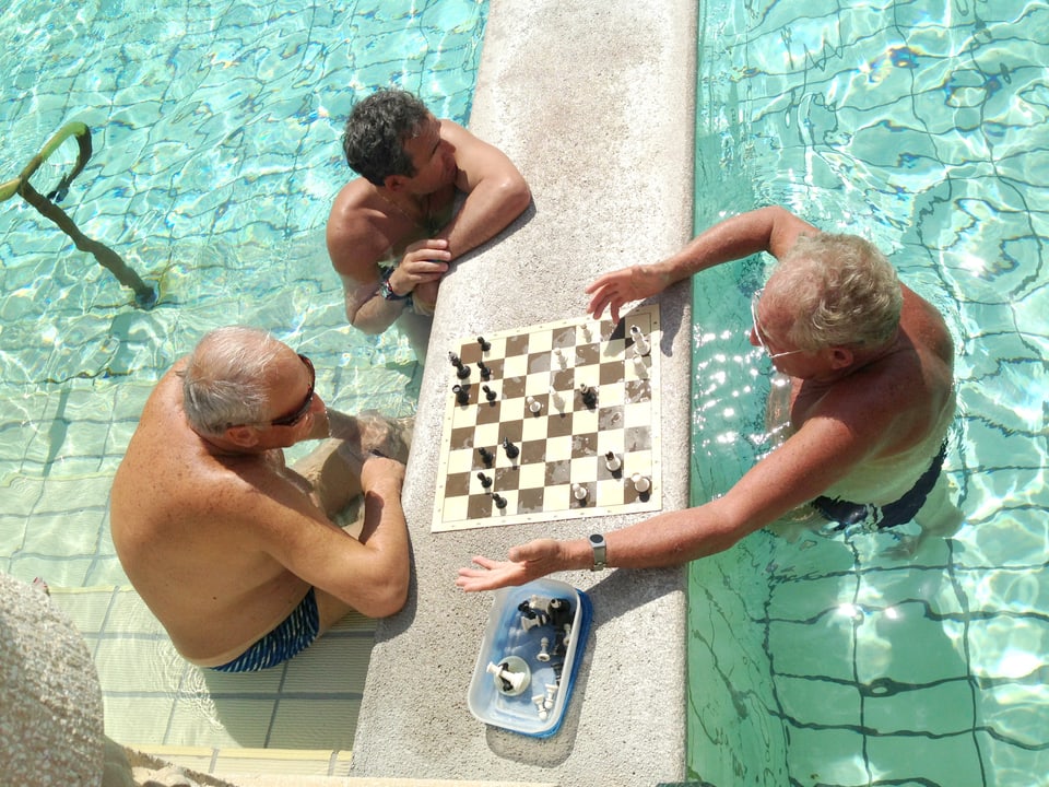 Drei Männer stehen im Wasser und spielen Schach.