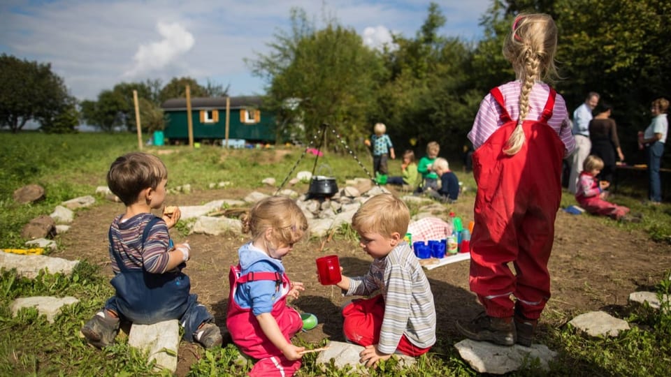 Kinder im Waldkindergarten sitzen rund um eine Feuerstelle und essen.