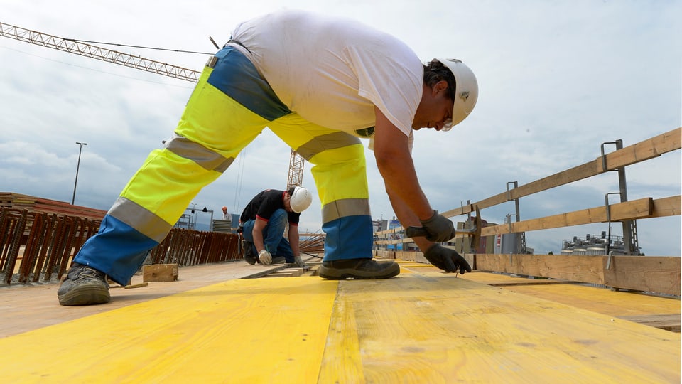 Bauarbeiter auf einer gelben Holzplatte. Er bückt sich.