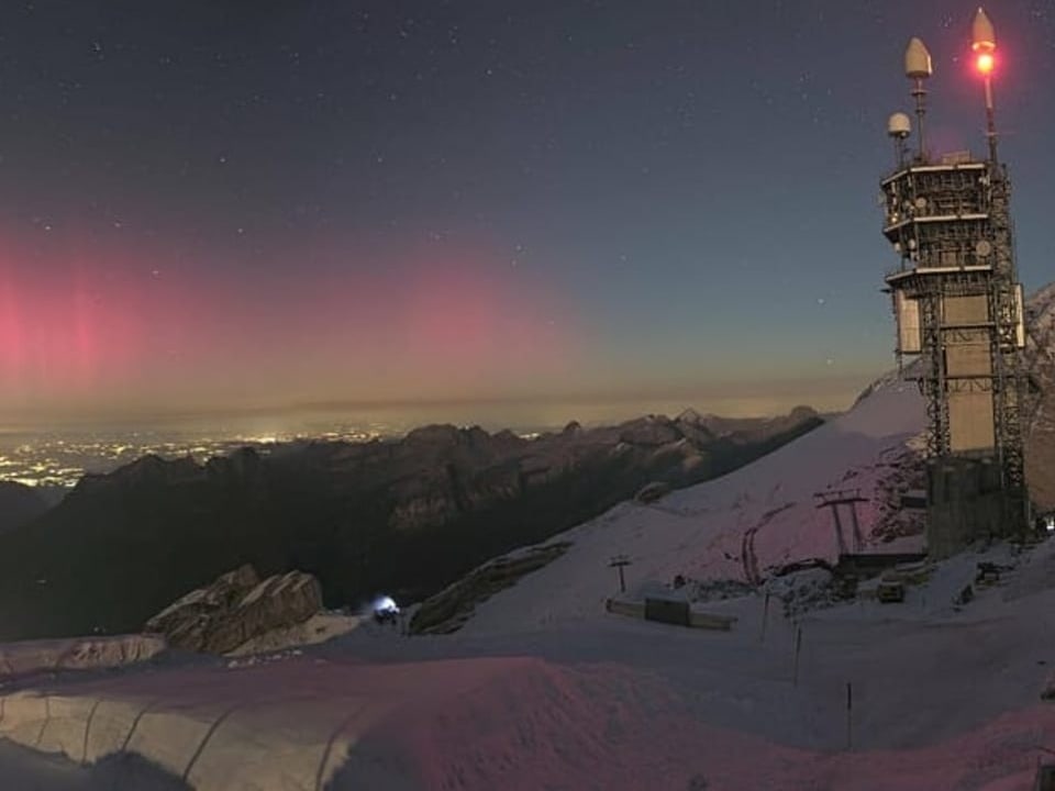 Blick von einem Gipfeln in den Nachthimmel mit rotem Licht am Horizont, dem Polarlicht. 