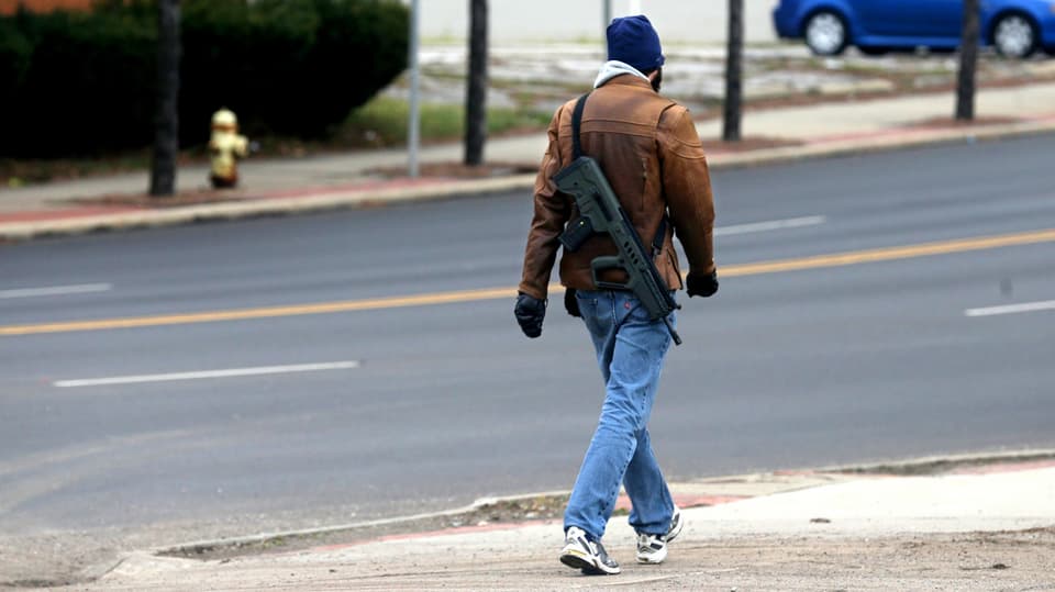 Mann von hinten, der mit einer Seriefeuerwaffe durch die Strassen spaziert.