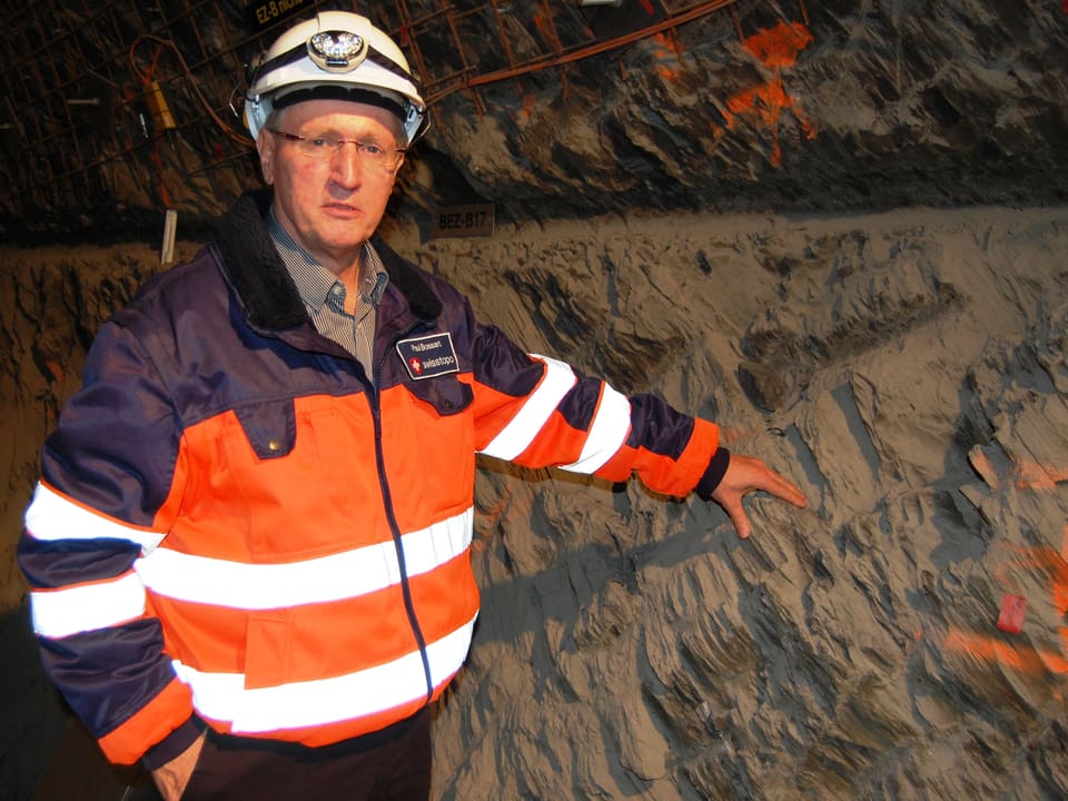 Mont Terri-Laborleiter Paul Bossart vor einer wunderschön geschichteten, dunkelgrauen Opalinuston-Schicht im Felslabor.