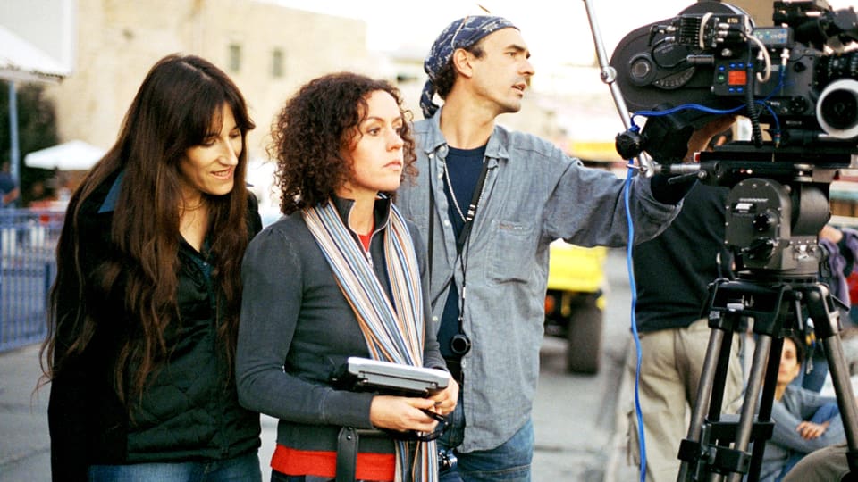 Zwei Frauen und ein Mann stehen hinter einer Filmkamera.
