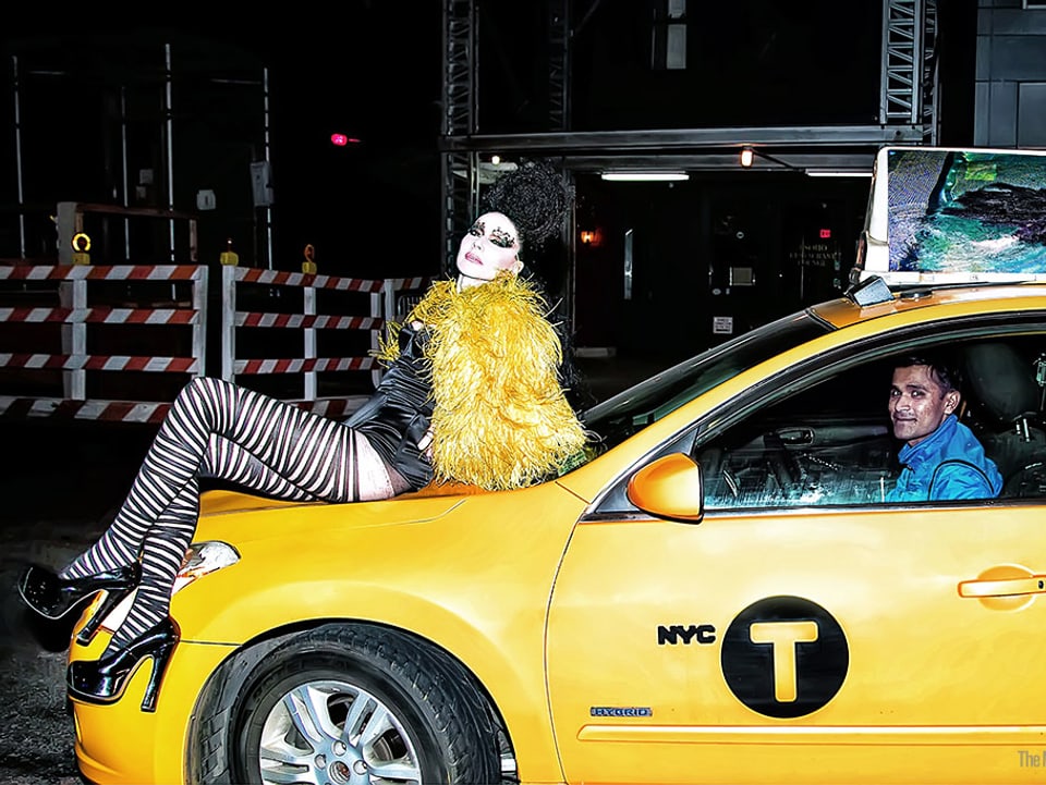 Frau in einem exaltierten Outfit auf der Motorhaube eines Taxis.