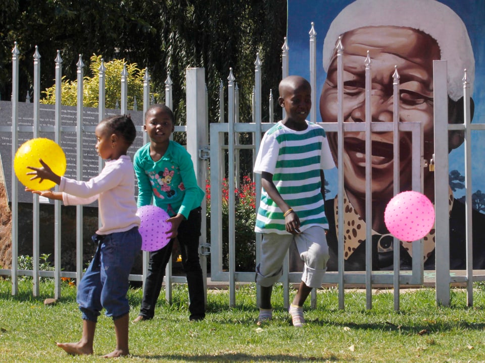 Auf eine Wand ist ein Portrait von Mandela gemalt, davor spielen Kinder mit bunten Bällen