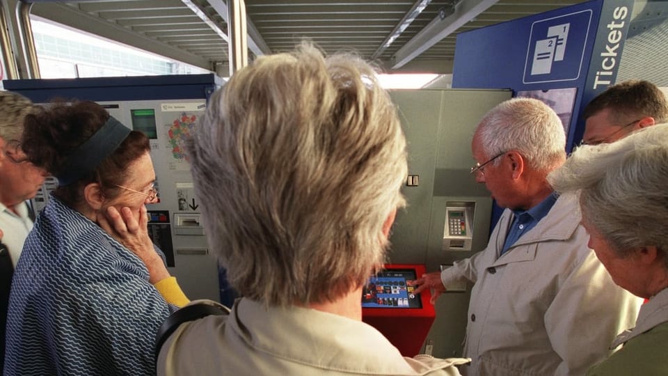 Ältere Menschen stehen um einen SBB-Ticketautomaten herum, ein Mann erklärt die Funktionen auf dem Bildschirm
