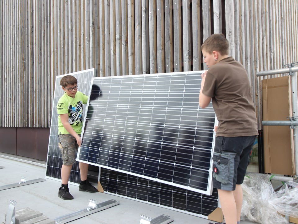 Zwei Jugendliche haben sorgfältig ein Solarpanel hoch.