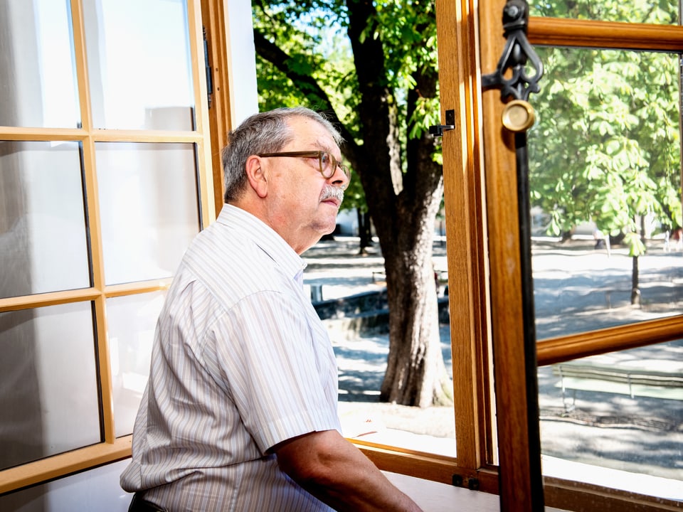 Ein älterer Herr mit Brille und Schnauz schaut aus dem geöffneten Fenster.