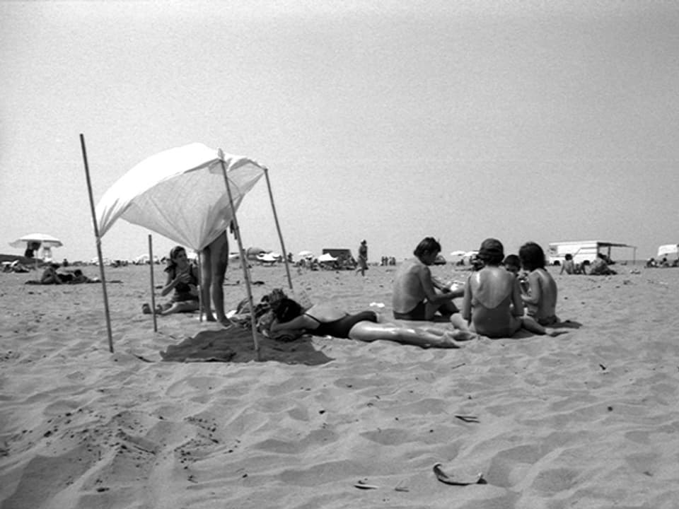 Strand mit einem Tuch, das Schatten spendet, Leute sitzen im Sand.