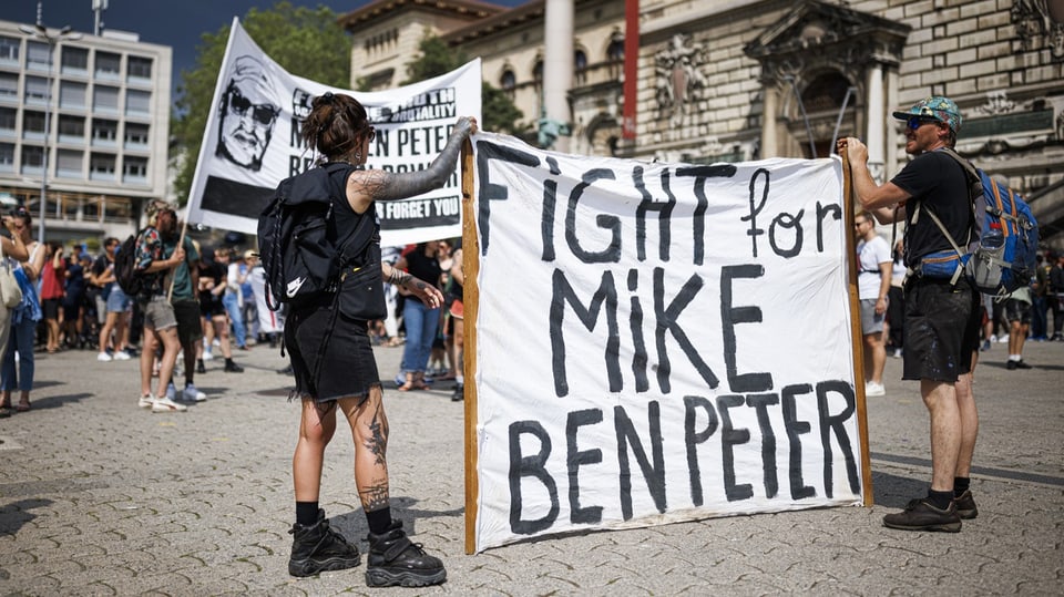 Eine Frau und ein Mann halten ein Transparent, auf dem steht «Fight for Mike Ben Peter».