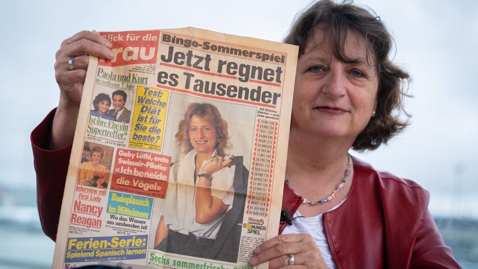 Frau in roter Lederjacke mit einer älteren Zeitung in der Hand. 