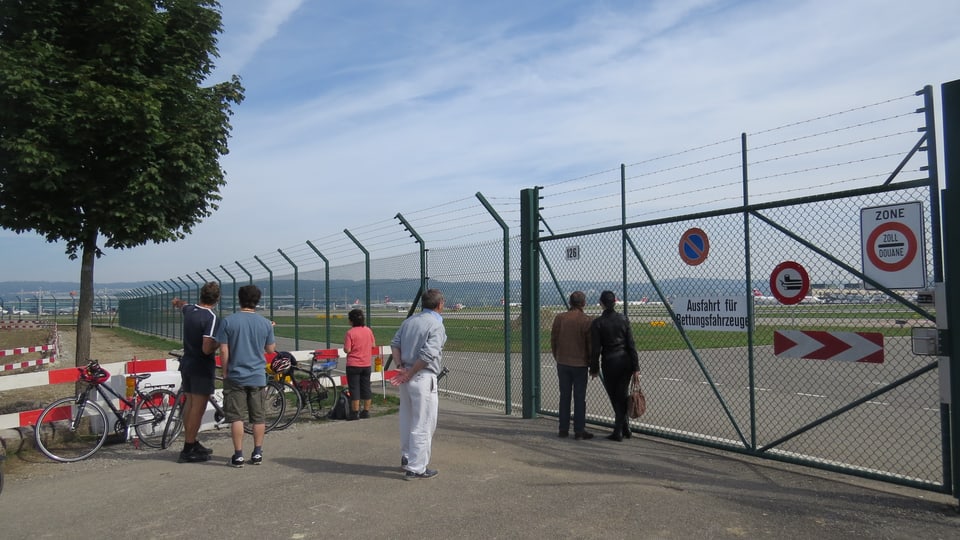 Menschen am Zaun zum Flughafengelände stehend