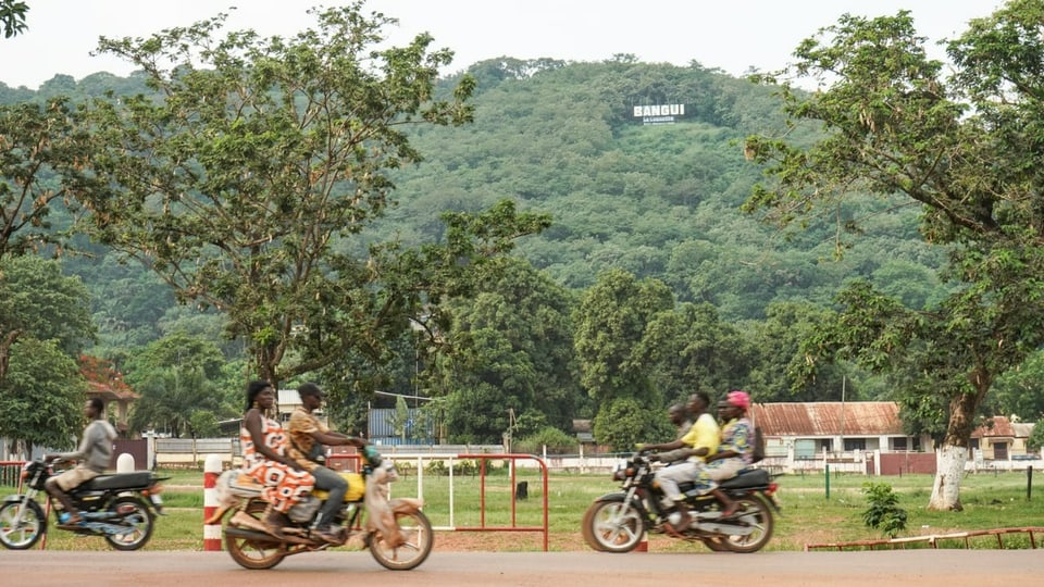 Motorradfahrer vor einem Hügel mit dem Schriftzug «Bangui»