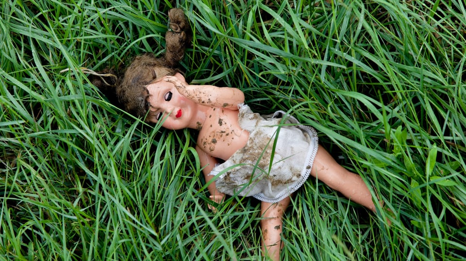 Eine verschmutzte Puppe liegt halb ausgezogen im Gras.