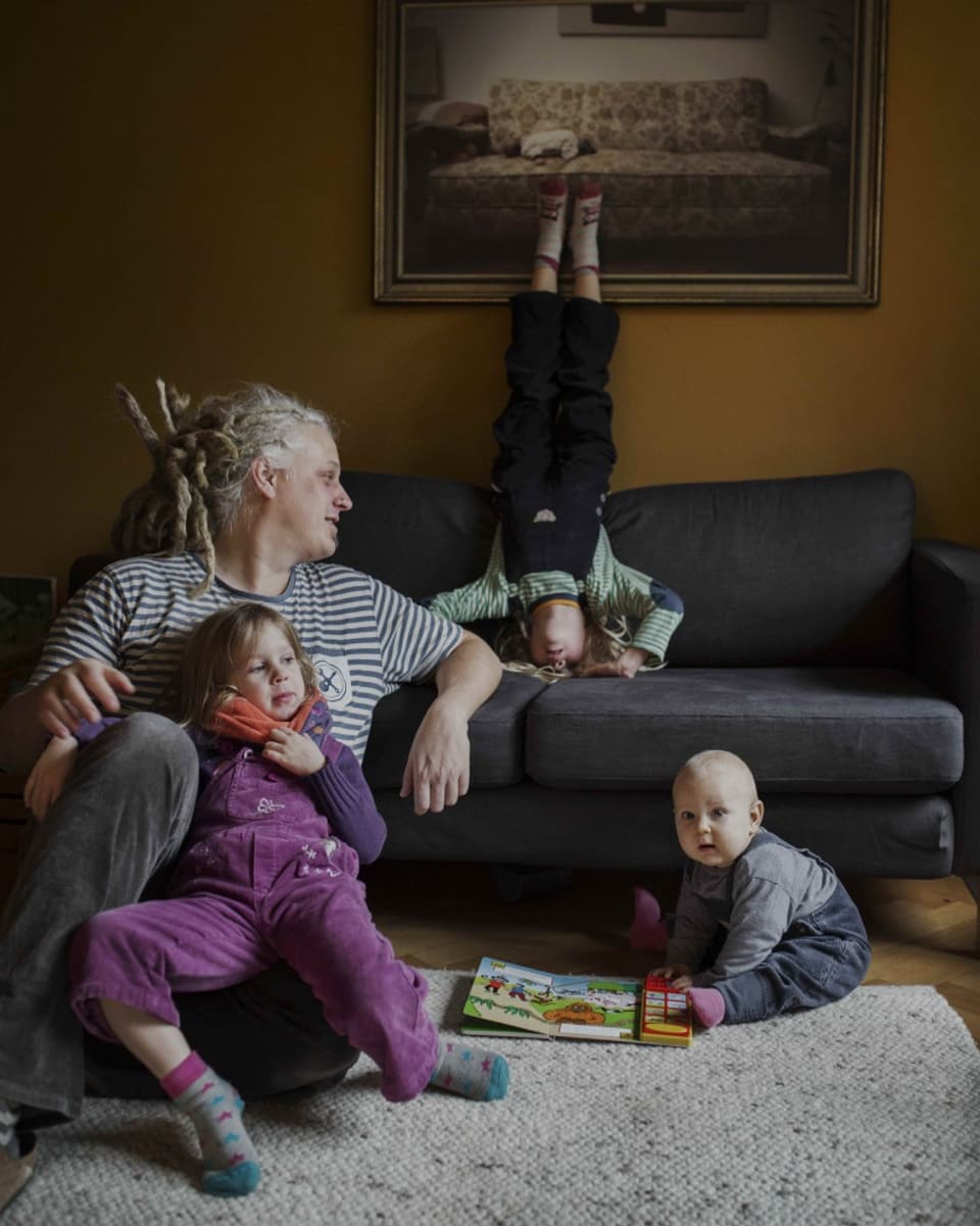 Ein Vater mit drei Kinder, eines macht auf dem Sofa den Kopfstand.