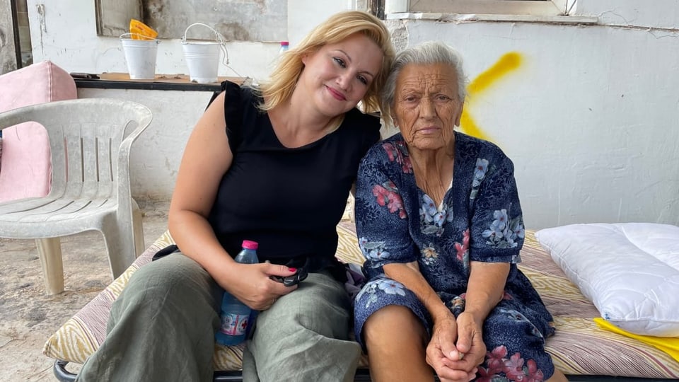 Die betroffene Frau und ihre Nichte sitzen für ein Foto zusammen auf dem Klappbett.