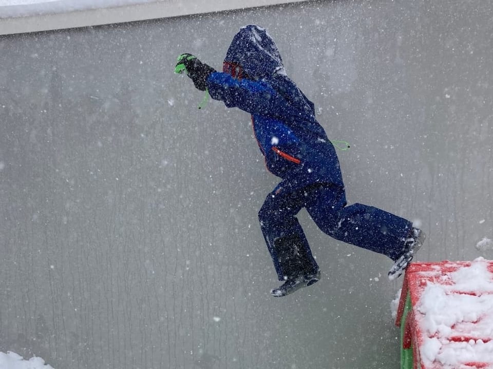 Ein Kind springt von einem Spielhaus in einen Schneehaufen.