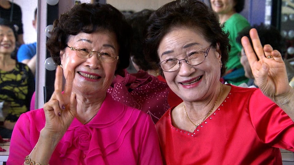 Zwei Südkoreanerinnen grinsen in die Kamera, mit den Fingern machen sie das Peace-Zeichen.