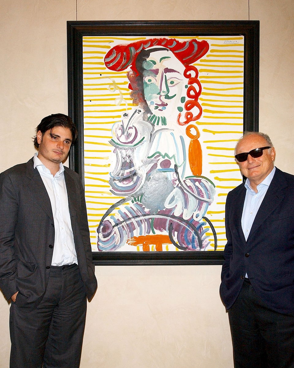 Ein jüngerer und ein älterer Mann posieren vor einem Bild von Picasso.