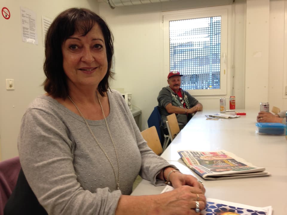 Chantal Zürcher, im Hintergrund sitzt ein Mann am Tisch, daneben zwei Bierdosen. 