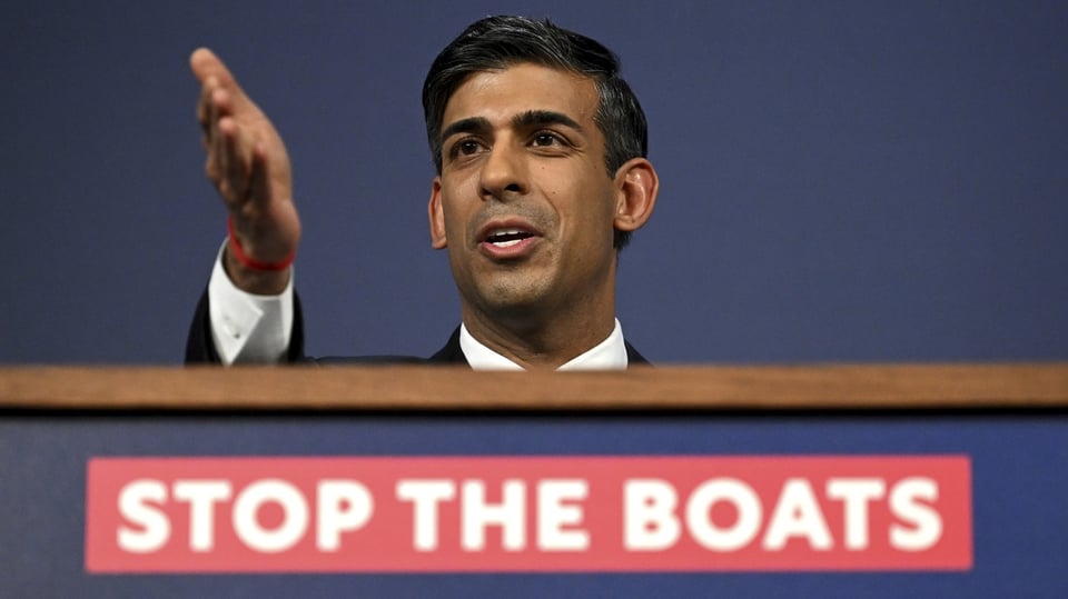 Der britische Premierminister Rishi Sunak, vor ihm ein Schild: Stoppt die Boote